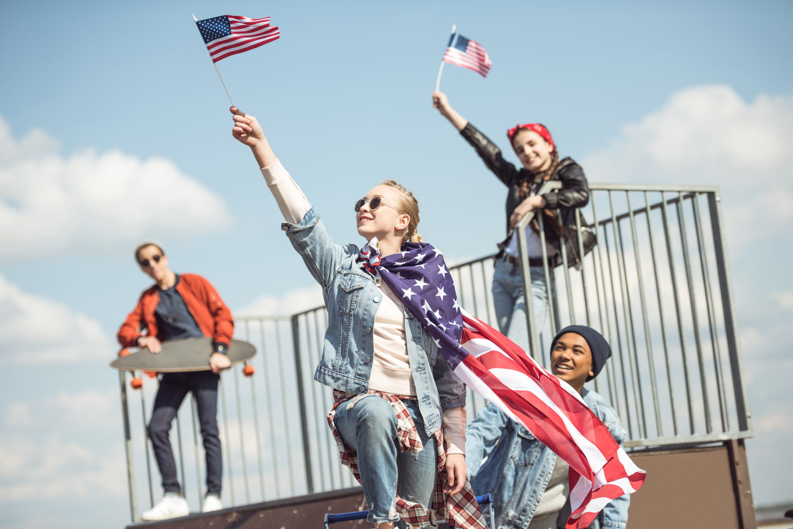 Teenagers group having fun together and waving american flags at skateboard park